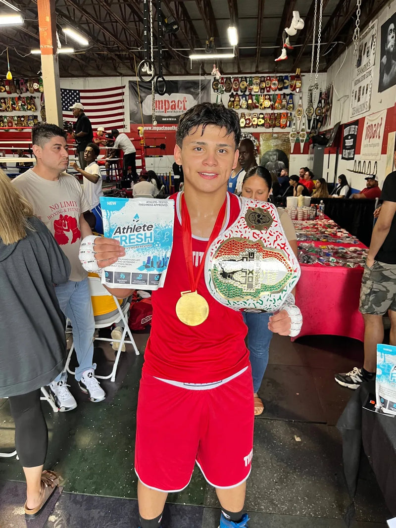 Champion boxer holding his belt, medal, and a bag of Athlete Fresh at a live boxing event